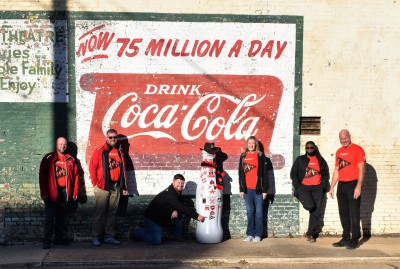 Paris heroes pose with the Recognition Roadtrip Bottle in front of the Coca-Cola mural at the Lamar Theater on Feb. 15, 2022. Located in downtown Paris, the Lamar Theater was built in 1929 and closed in 1963. After its closing, sheet metal was added to the building, hiding the theater for over half a century. But during renovations in 2018, contractors removed the metal to reveal the old brick theater still intact – complete with this vintage Coca-Cola mural painted on the side!